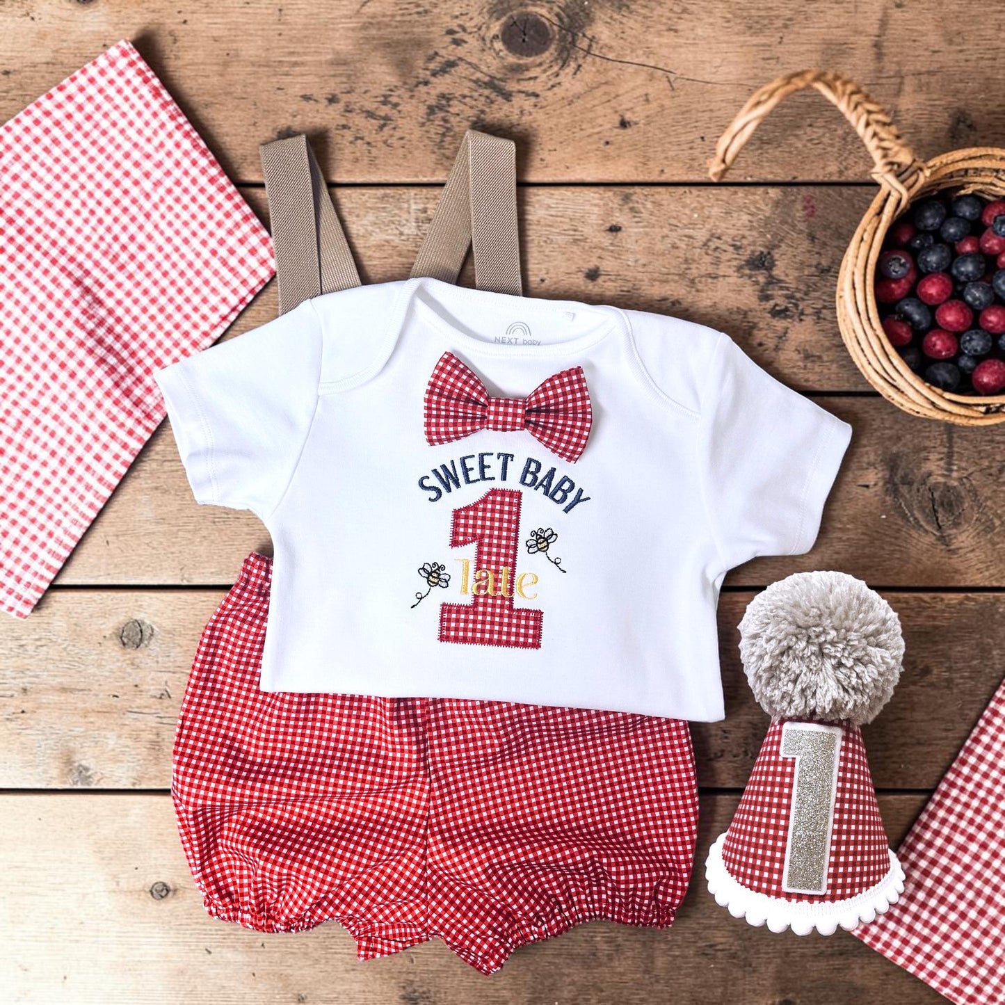 Handmade personalised red gingham first birthday outfit with embroidered bodysuit, suspenders and matching birthday hat for cake smash photos.
