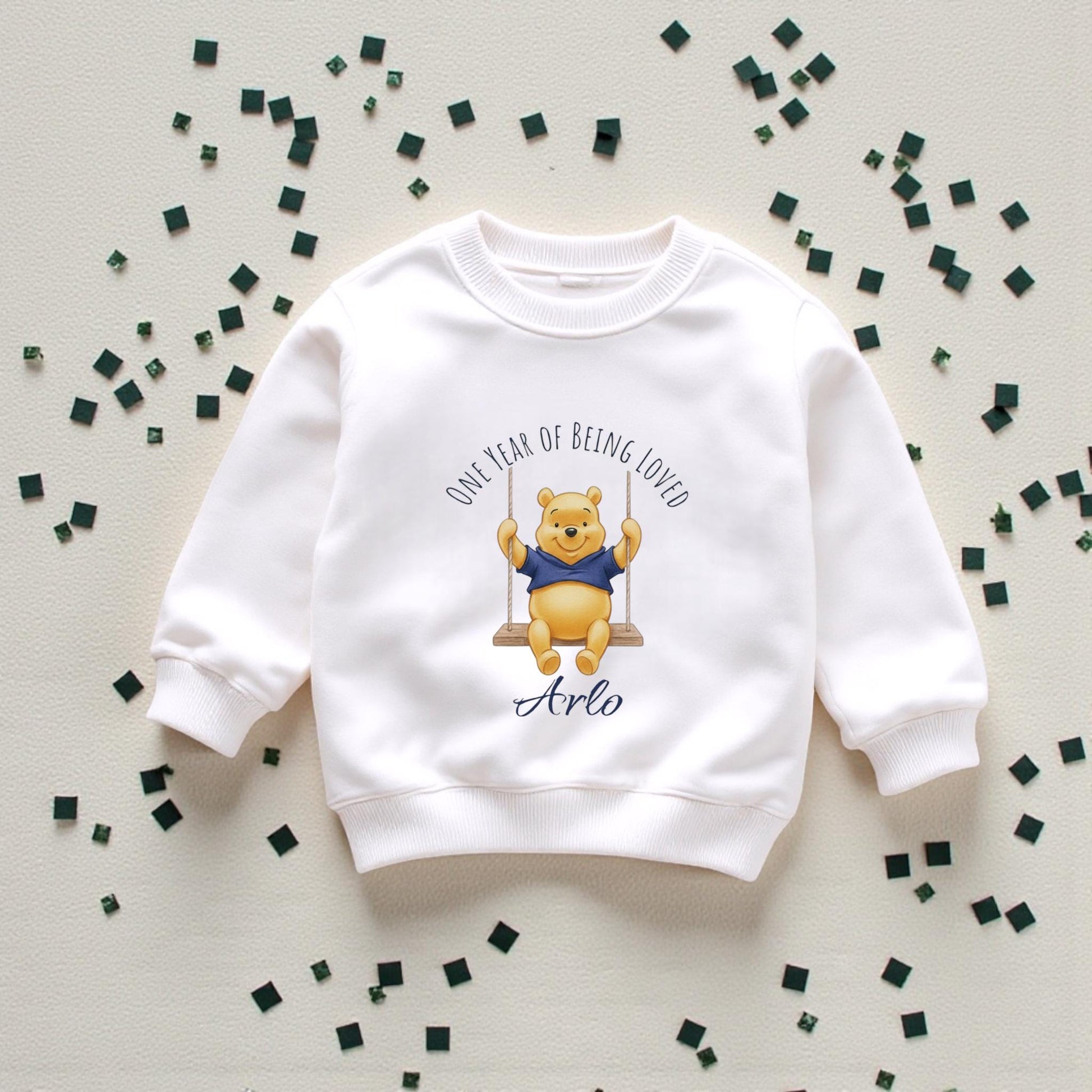 Personalised baby boy birthday sweatshirt with honey bear illustration and name, displayed flat on wooden background.