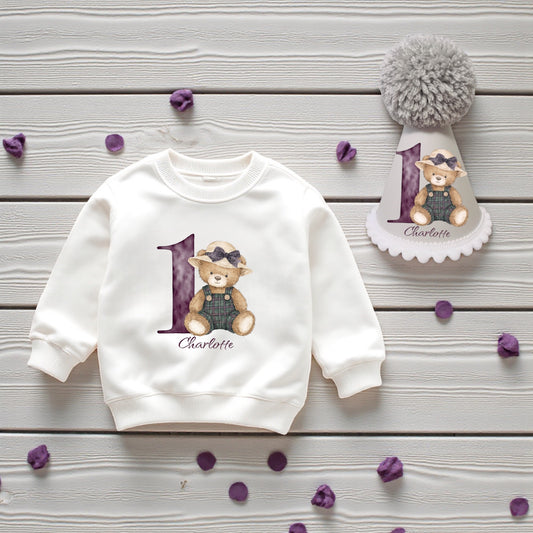 White sweatshirt with purple teddy print and matching handmade birthday hat styled on wood with purple confetti.