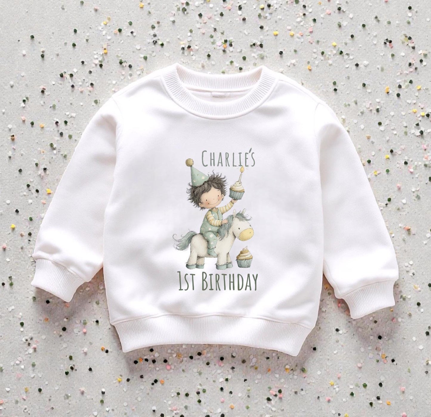 Personalised baby first birthday set with printed sweatshirt  displayed on neutral background with decorative confetti.