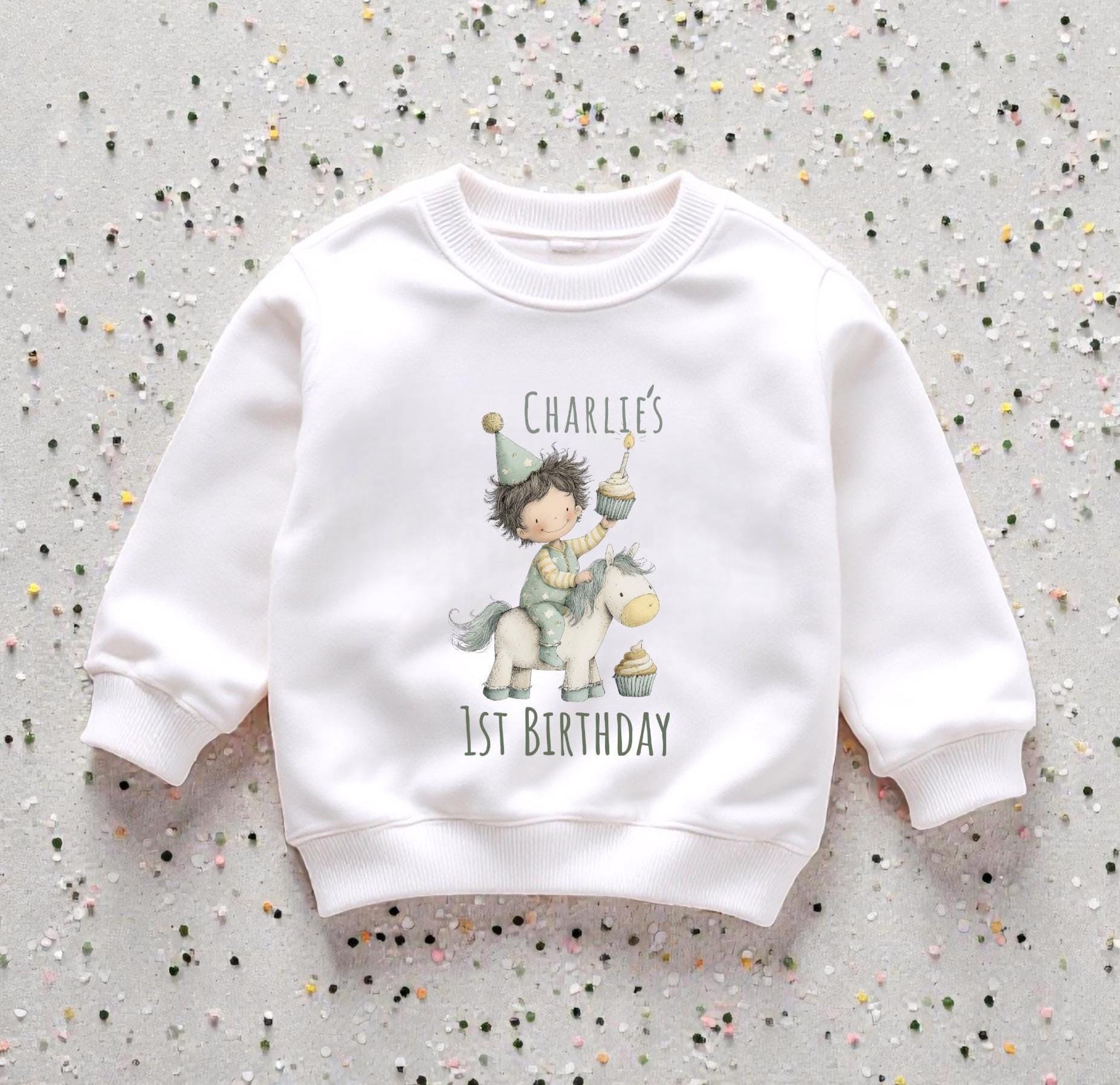 Personalised baby first birthday set with printed sweatshirt  displayed on neutral background with decorative confetti.