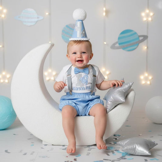 Blue first birthday outfit for baby boy with suspenders and bow tie, space theme photoshoot with planets and stars