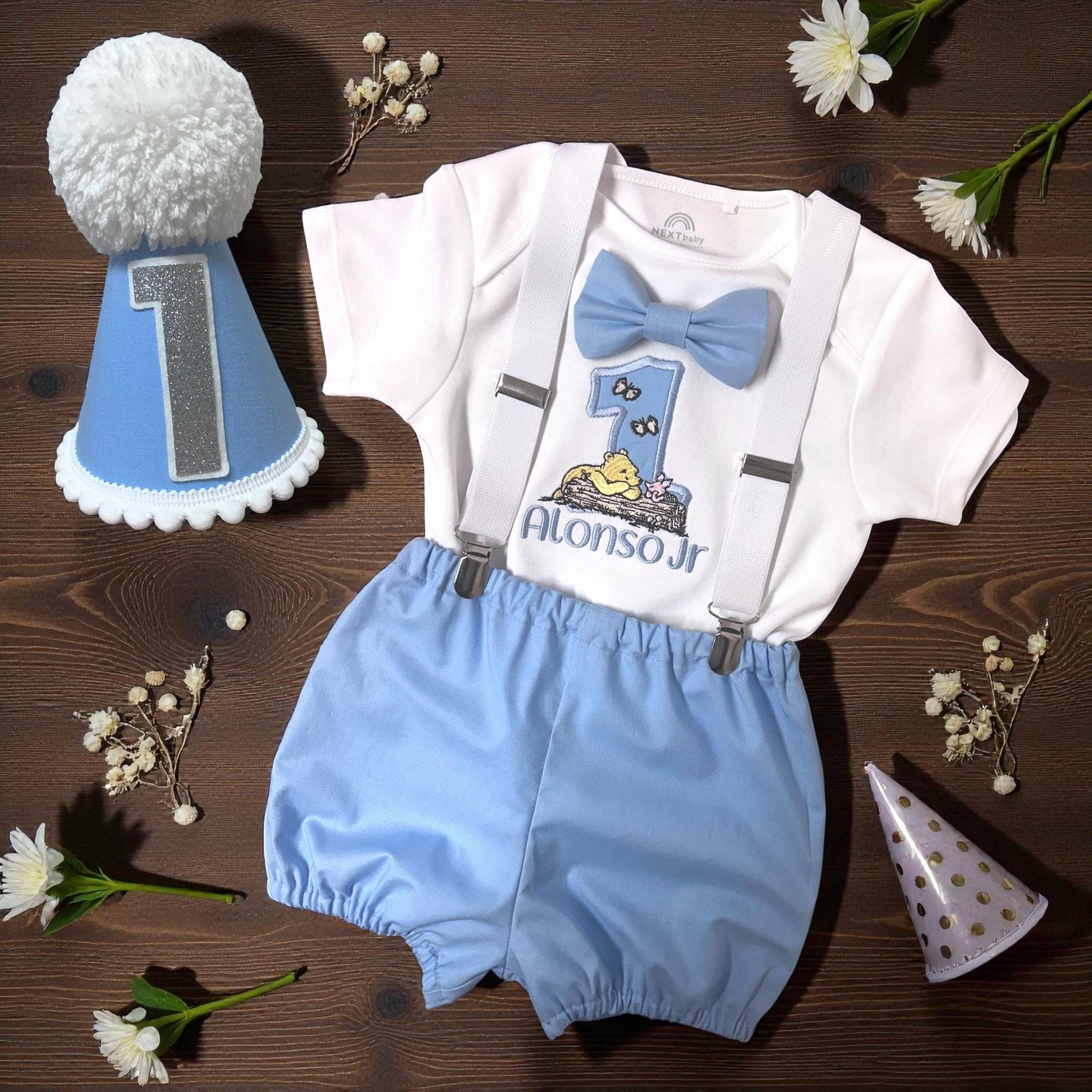 Pooh themed 1st birthday photo prop outfit for baby boy with blue party hat, honey pot backdrop, and woodland decorations