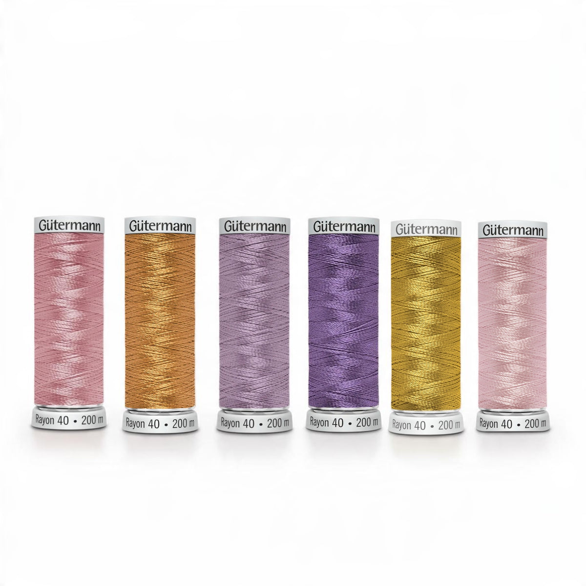 Six spools of Gutermann sewing thread used on the sweatshirt - in assorted pastel and metallic shades, including pink, orange, lavender, gold, and light pink, arranged in a row on a white background.