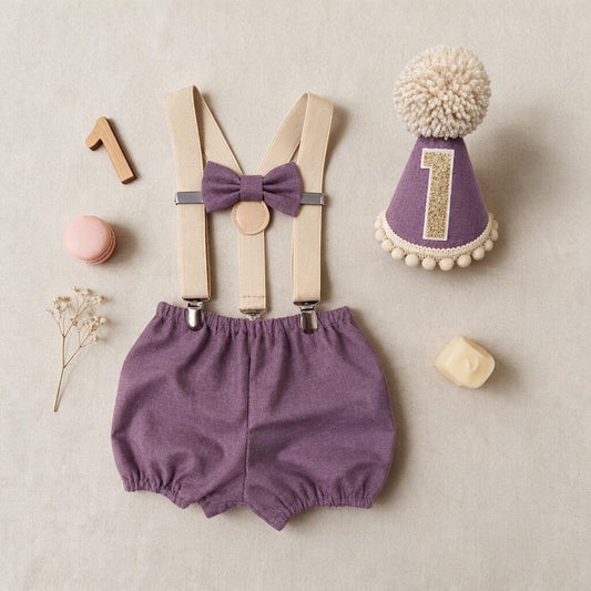 Handmade mauve birthday cake smash outfit with Moda Bella Solids cotton bloomer shorts, matching bow, beige braces and party hat with champagne glitter number one and fluffy stone-coloured pom-pom.
