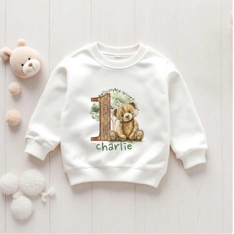 White sweatshirt with teddy bear design and text on a light wooden surface