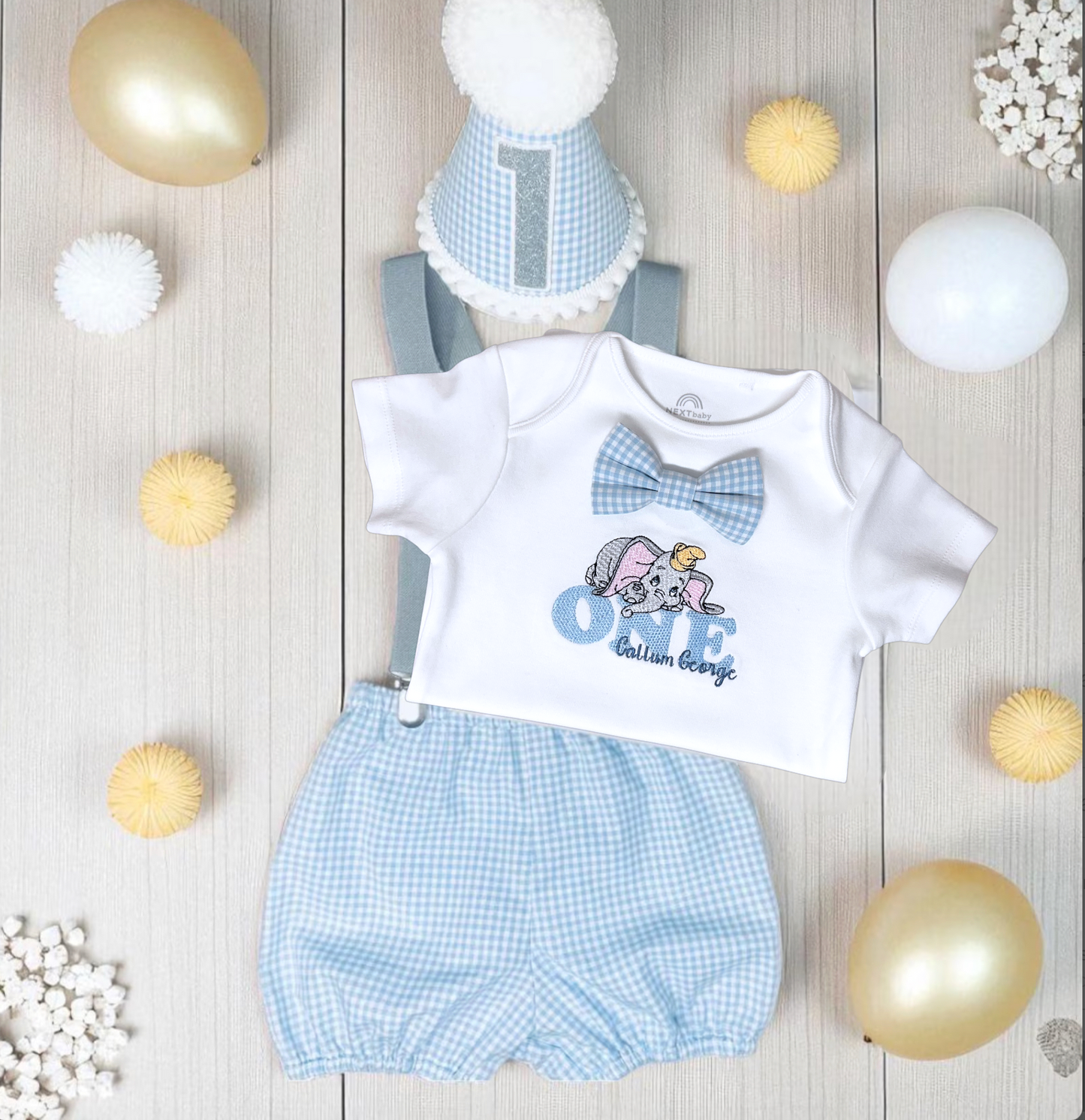 Baby outfit with white shirt, blue checkered shorts, and matching hat on a wooden surface with decorative lights.