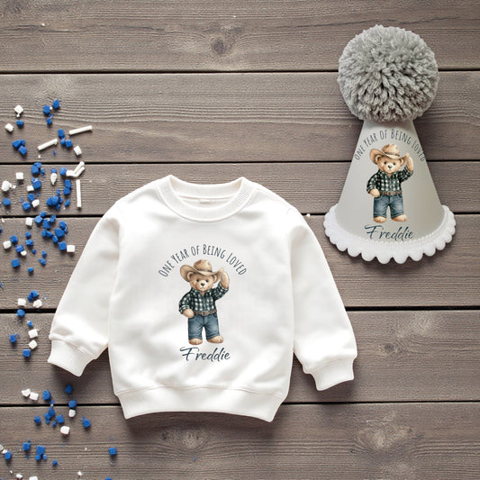 White sweatshirt with bear design and party hat on wooden surface