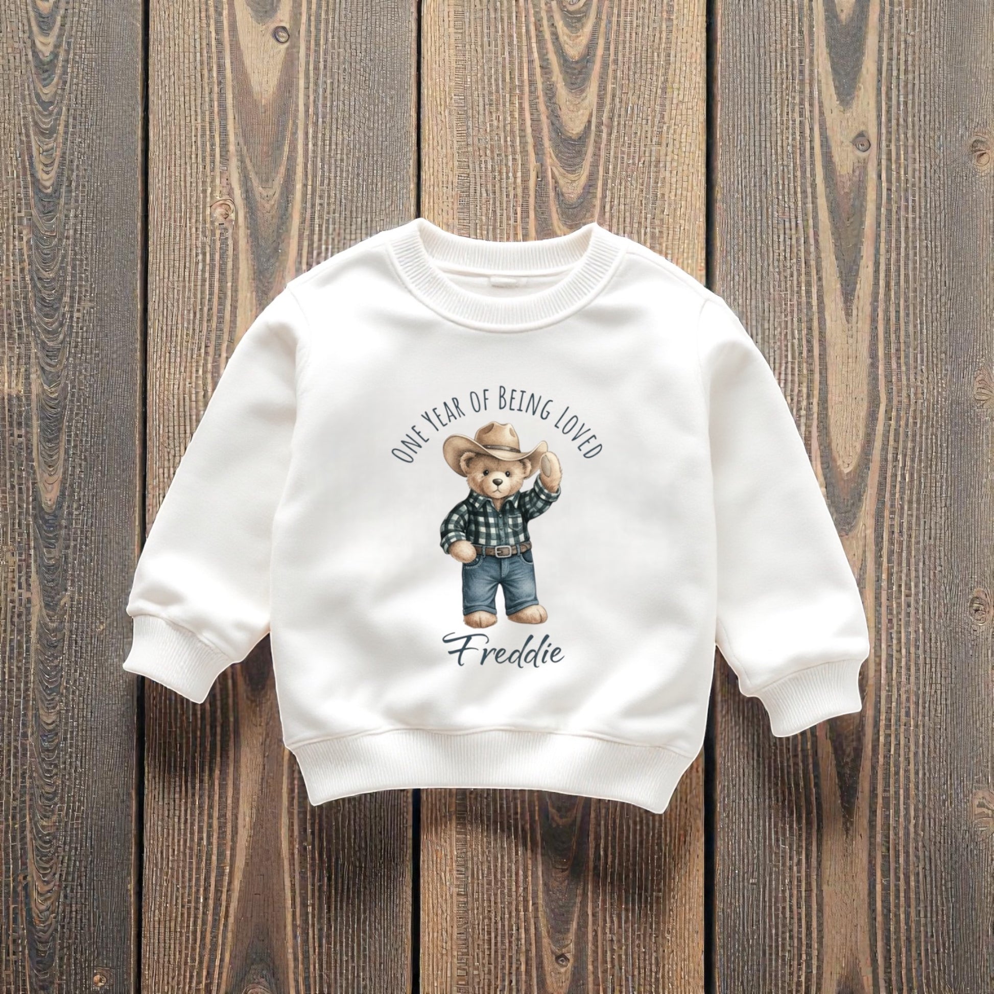 White sweatshirt with a bear graphic and text on a wooden background