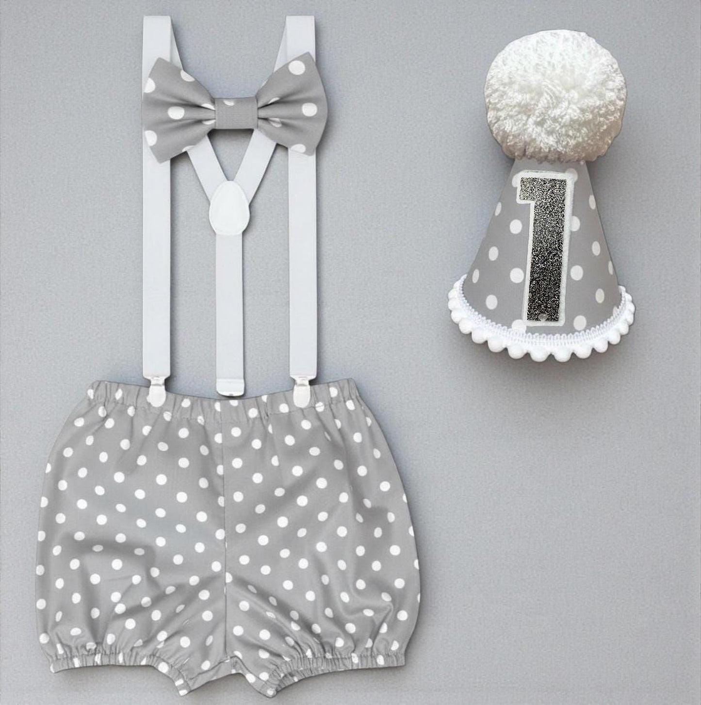 a gray and white polka dot outfit consisting of shorts and a bow tie, along with a gray and white polka dot birthday hat with the number 1 on it.