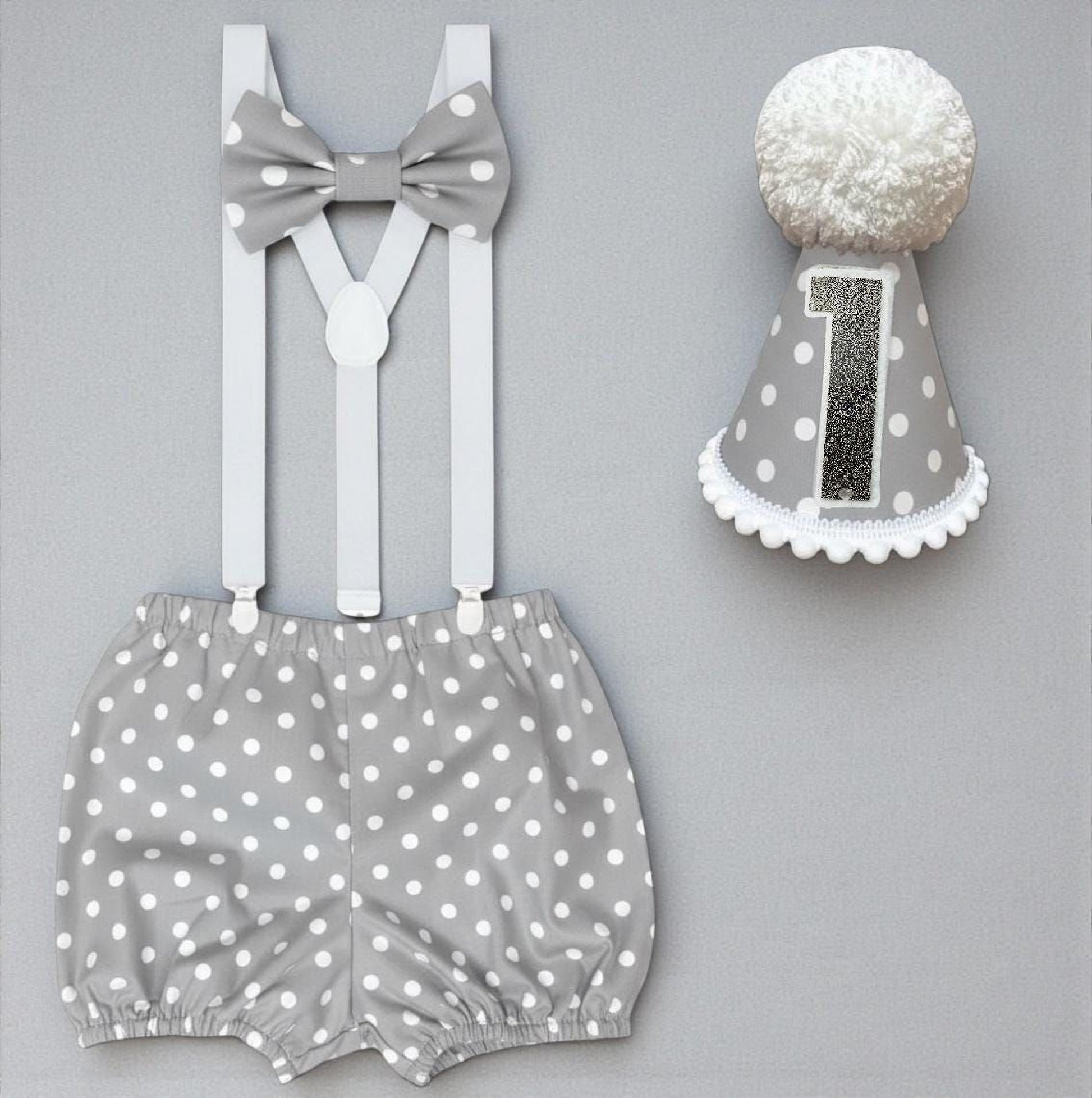 a gray and white polka dot outfit consisting of shorts and a bow tie, along with a gray and white polka dot birthday hat with the number 1 on it.