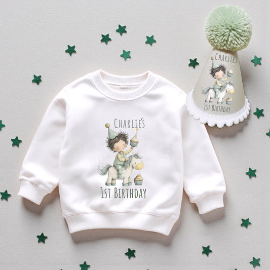 Personalised baby first birthday set with printed sweatshirt and handmade pom-pom party hat, displayed on neutral background with decorative stars.