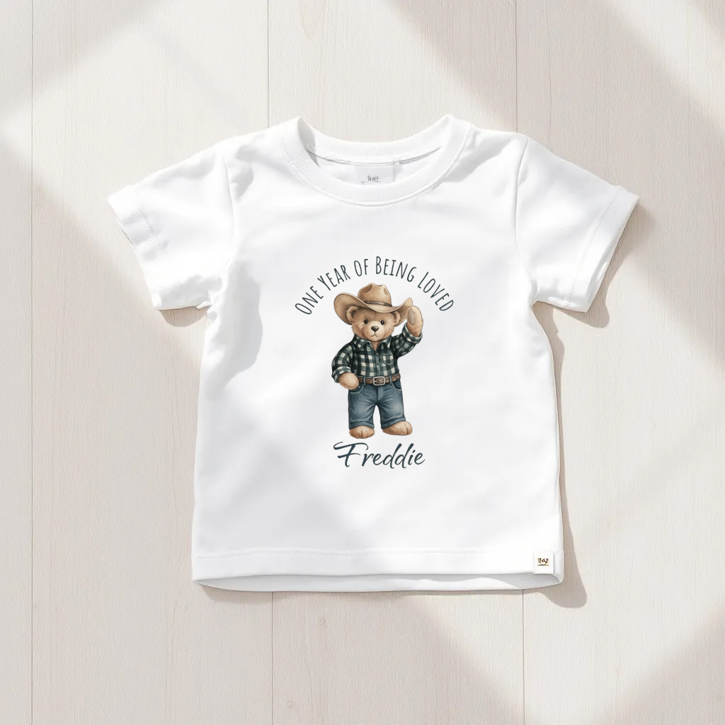 White t-shirt with a teddy bear graphic and text on a light wooden surface