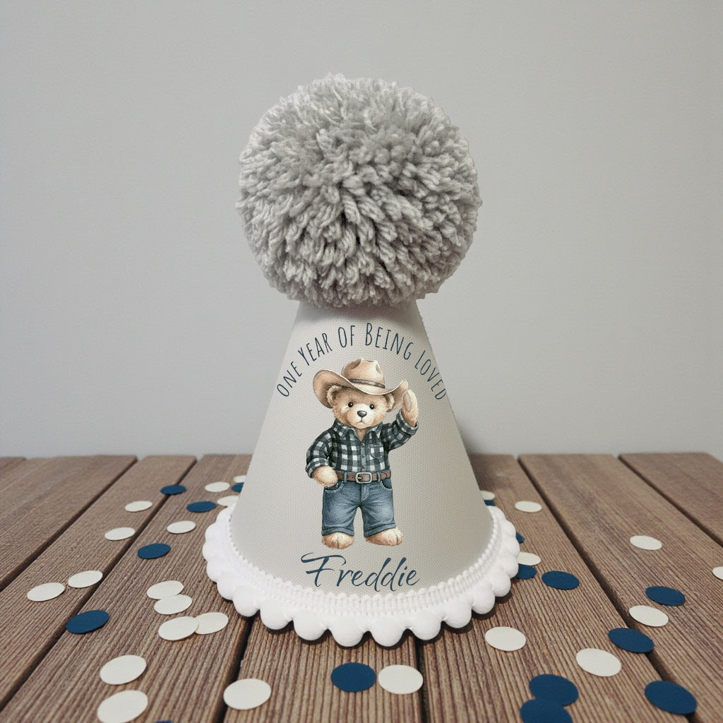 Birthday hat with teddy bear design and text on a wooden table with confetti.