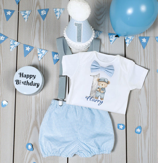 Personalised blue gingham teddy bear birthday outfit with printed bodysuit, bloomers, braces and handmade party hat displayed on wooden background.