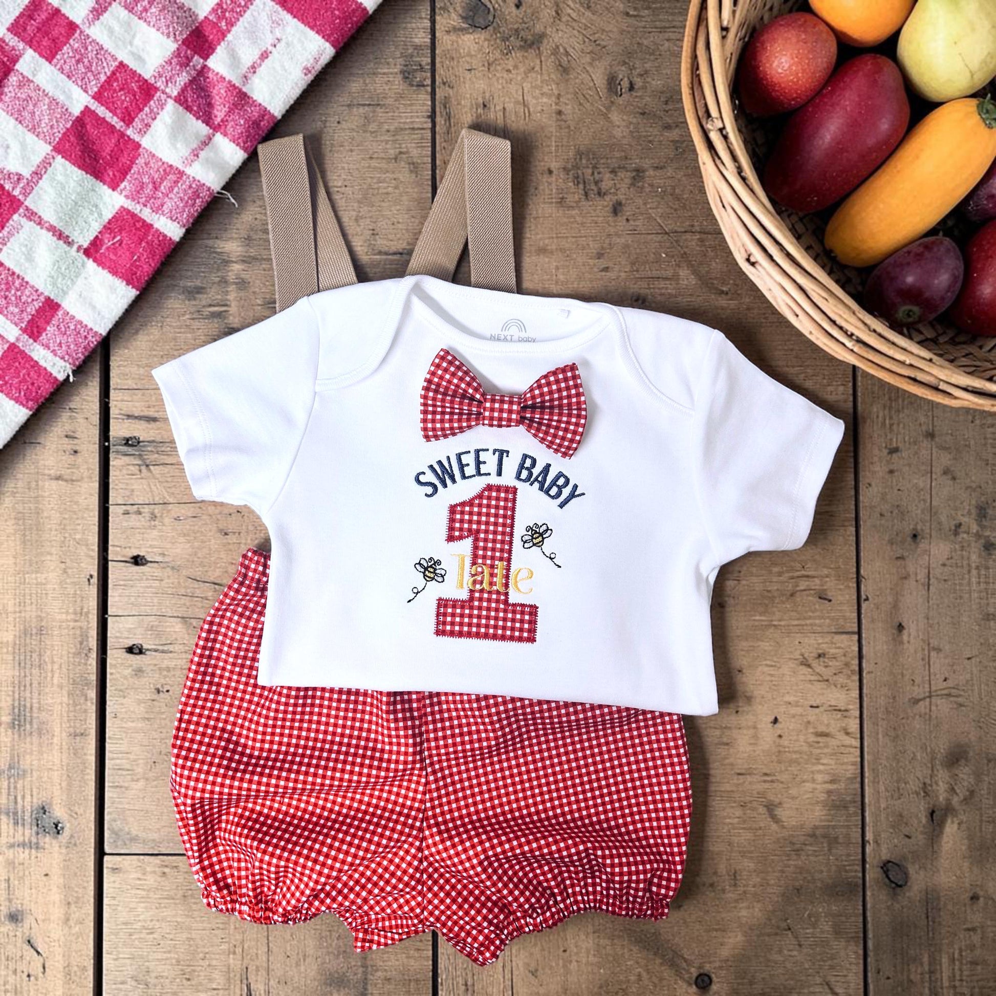 Handmade personalised red gingham first birthday outfit with embroidered bodysuit, suspenders and matching birthday hat for cake smash photos.