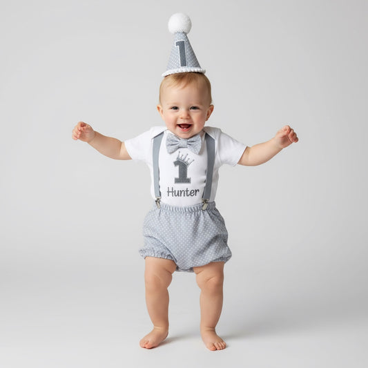 Baby wearing a white shirt with '1 Hunter' printed on it, gray suspenders, and gray shorts, standing against a plain background.