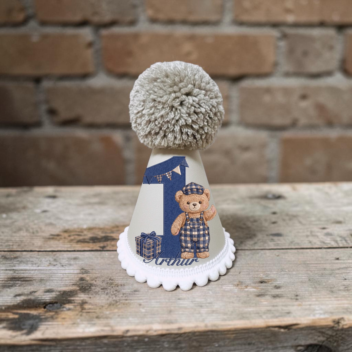 Personalised teddy bear birthday hat for baby boy with navy check details, birthday number, child’s name and large taupe yarn pom pom