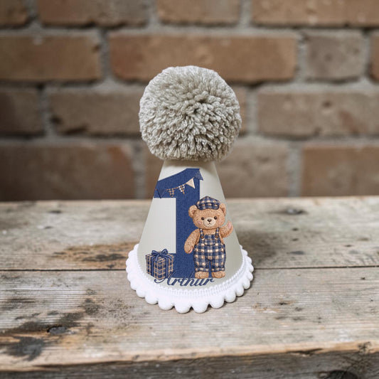 Personalised teddy bear birthday hat for baby boy with navy check details, birthday number, child’s name and large taupe yarn pom pom