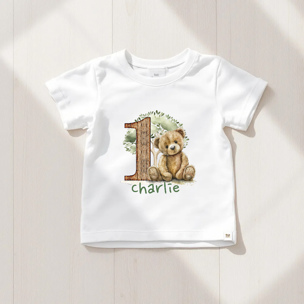 White t-shirt with a teddy bear design and the number '1' on a wooden surface